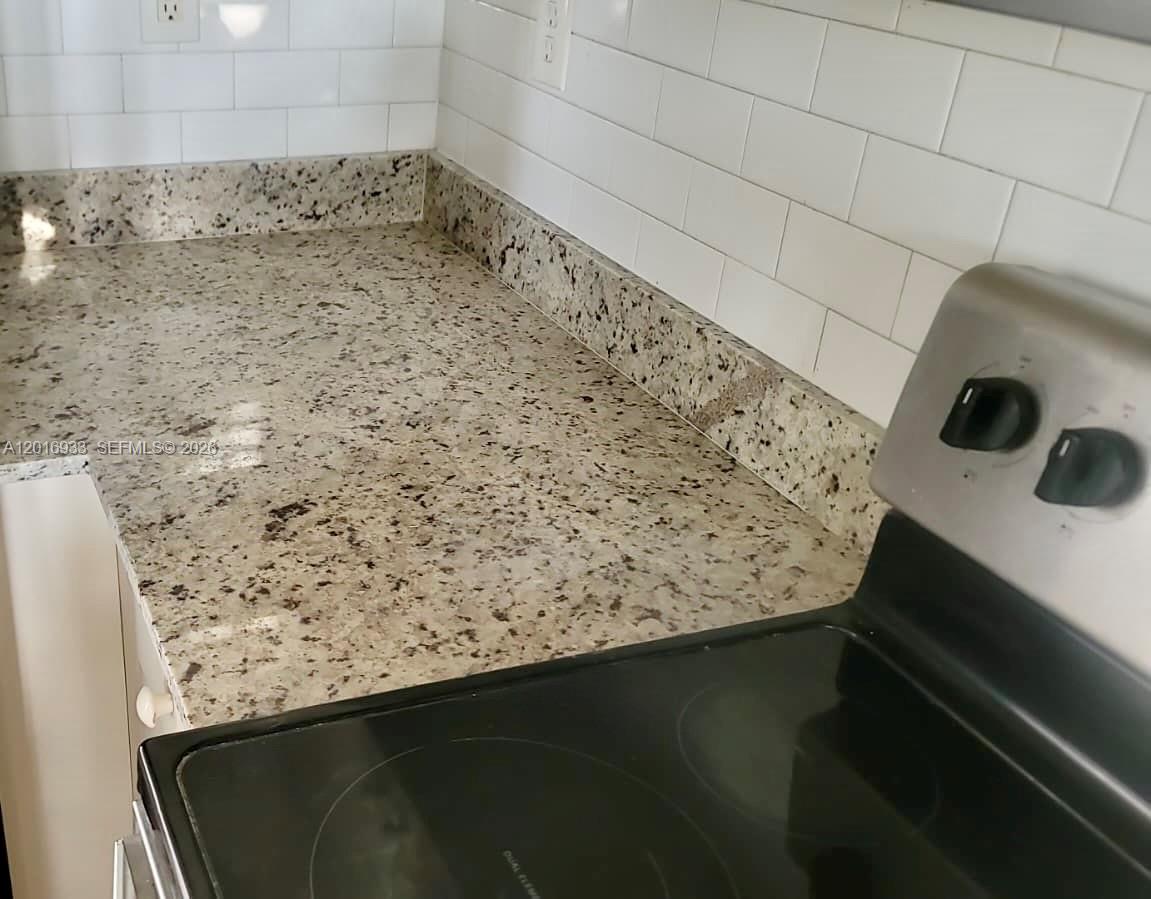 A kitchen features granite countertops, a white subway tile backsplash, and a black electric stove — HOMESTEAD, FL