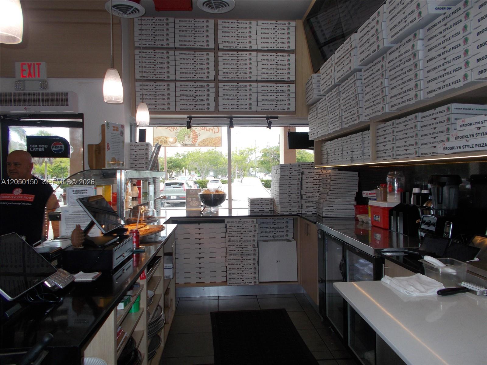 The interior of a pizza restaurant features stacks of branded pizza boxes and a counter — 8237 SW 124th St, Pinecrest FL 33156, PINECREST, FL