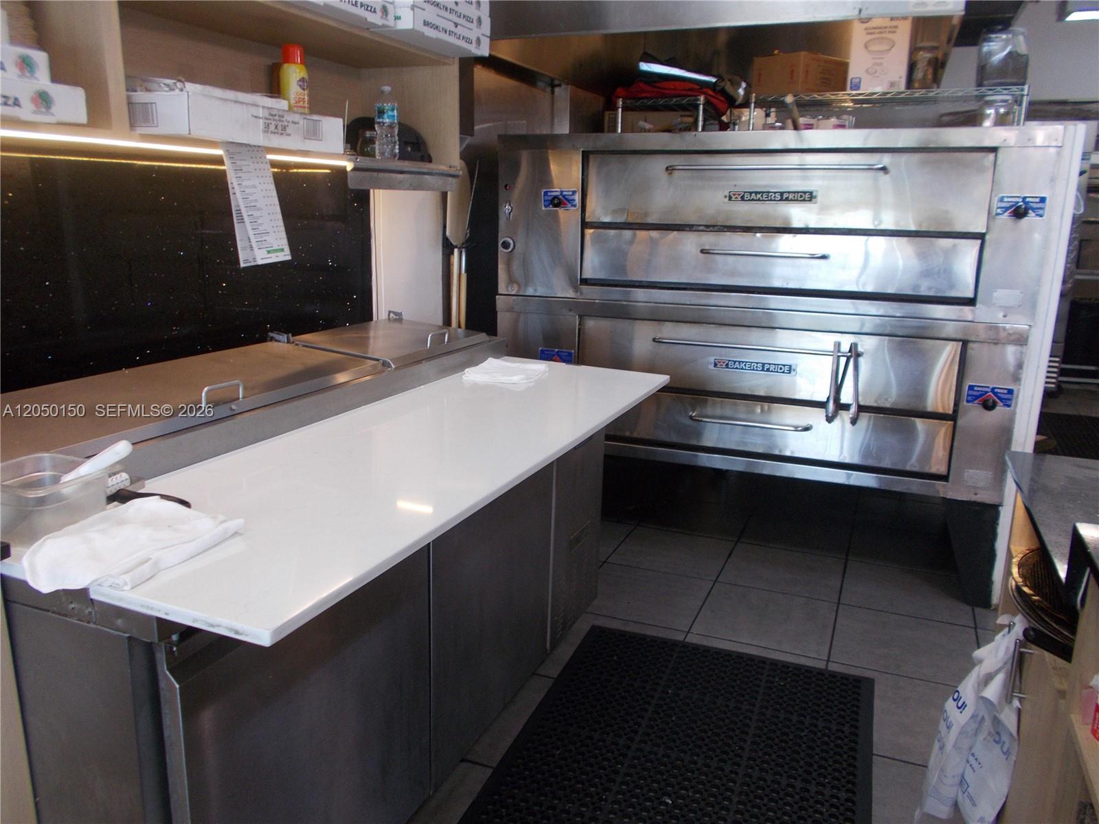 A commercial kitchen features a stainless steel pizza oven, a white prep counter, and shelving — 8237 SW 124th St, Pinecrest FL 33156, PINECREST, FL