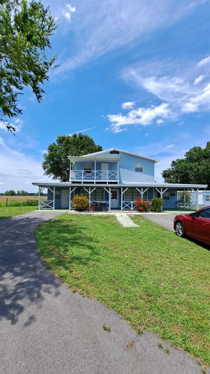 A two-story light blue house with a wrap-around porch and a second-story balcony — 6275 Us Highway 441 SE, Okeechobee FL 34974, OKEECHOBEE, FL