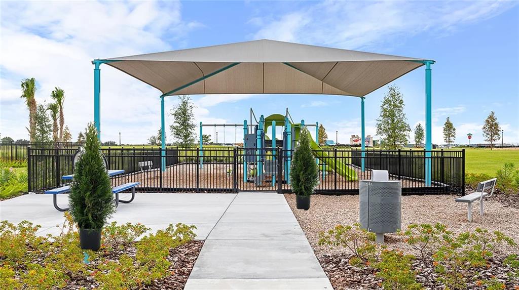 A playground with a large shade structure, metal fencing, and landscaping sits on a sunny day — 315 CASTLEVIEW DRIVE, DAVENPORT, FL