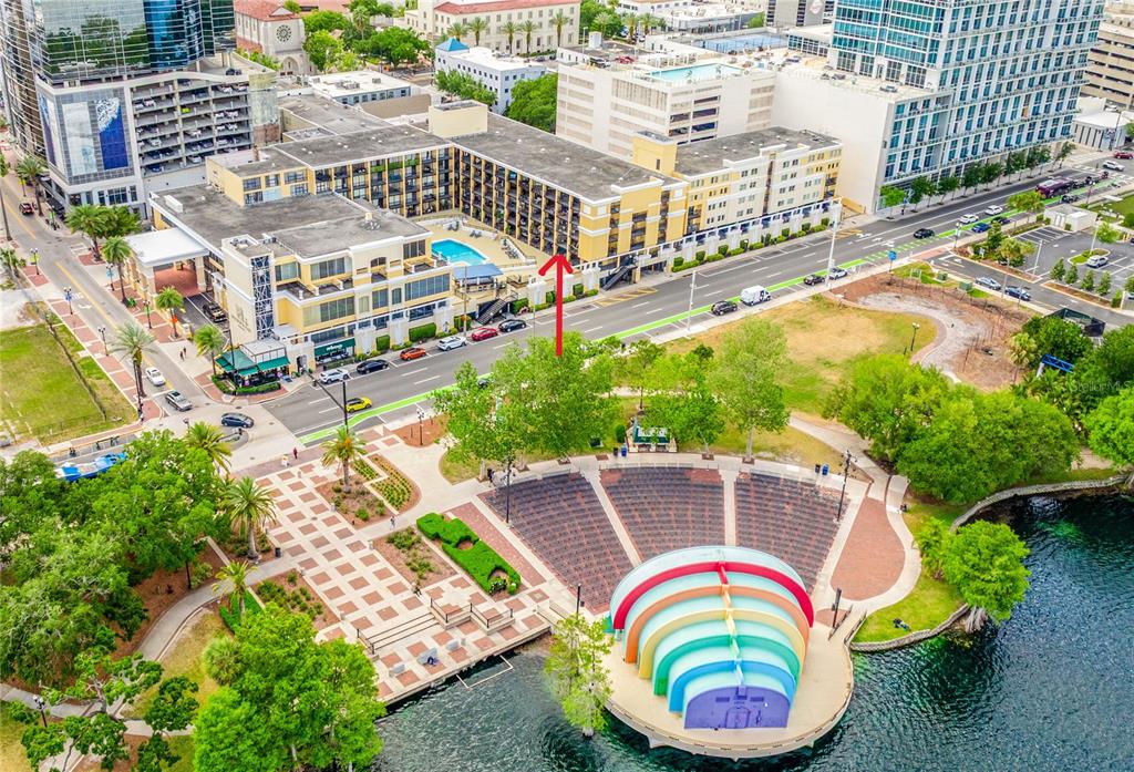 An aerial view shows a yellow hotel building across from a lakeside park and amphitheater — 151 E WASHINGTON STREET UNIT 218, ORLANDO, FL