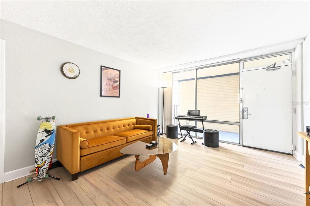 A living room with light wood floors, a mustard velvet sofa, and a glass-topped table — 151 E WASHINGTON STREET UNIT 218, ORLANDO, FL