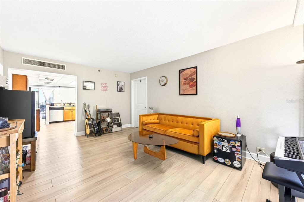 A living room features a mustard yellow velvet sofa, a glass coffee table, and wood-look flooring — 151 E WASHINGTON STREET UNIT 218, ORLANDO, FL