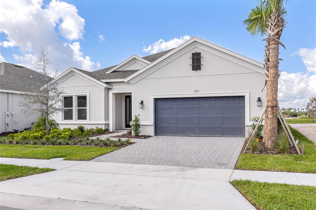 A single-story house with a gray garage door, light-colored stucco walls, and a palm tree — 992 TASSLEFLOWER TRAIL, ST CLOUD, FL