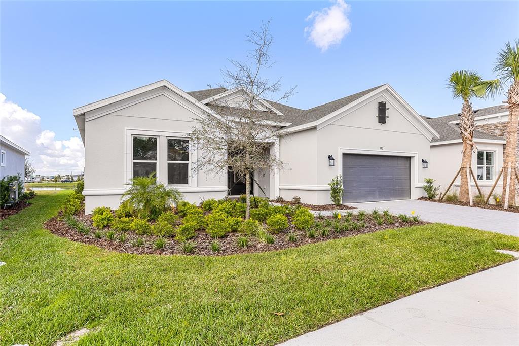 A single-story house with a gray garage, light-colored stucco exterior, and landscaped front yard — 992 TASSLEFLOWER TRAIL, ST CLOUD, FL