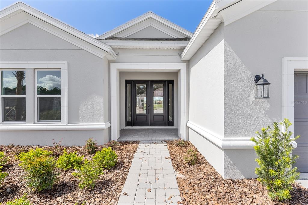 The front exterior of a house features a paved walkway leading to double glass doors — 992 TASSLEFLOWER TRAIL, ST CLOUD, FL
