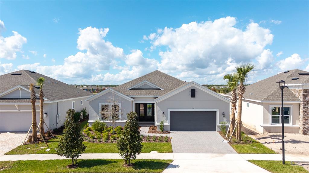A single-story suburban house with a gray garage, light-colored stucco exterior, and palm trees — 992 TASSLEFLOWER TRAIL, ST CLOUD, FL