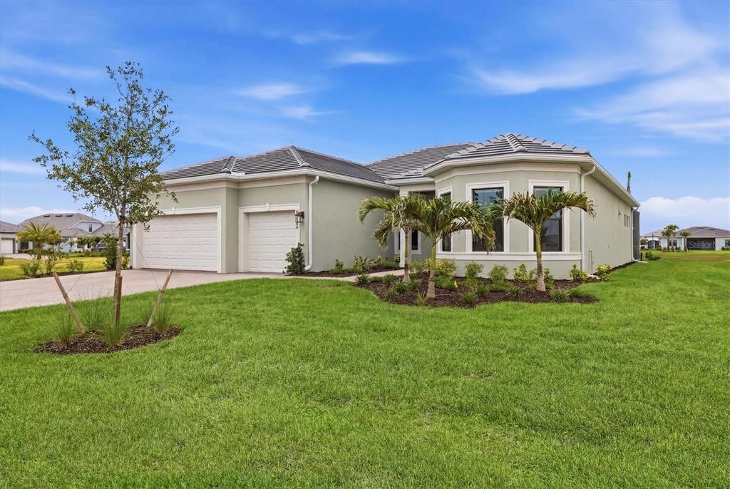A single-story house with a two-car garage, light green stucco exterior, and palm tree landscaping — 4923 EMPIRE LANDING RUN, BRADENTON, FL