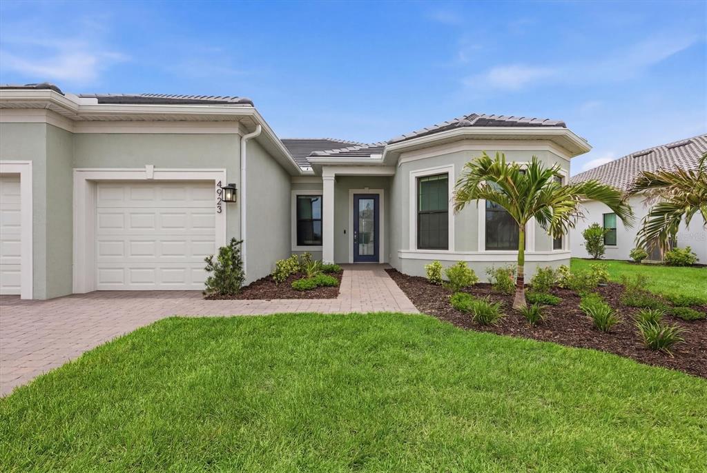 A single-story house with a light green exterior, a paved driveway, and a small palm tree — 4923 EMPIRE LANDING RUN, BRADENTON, FL