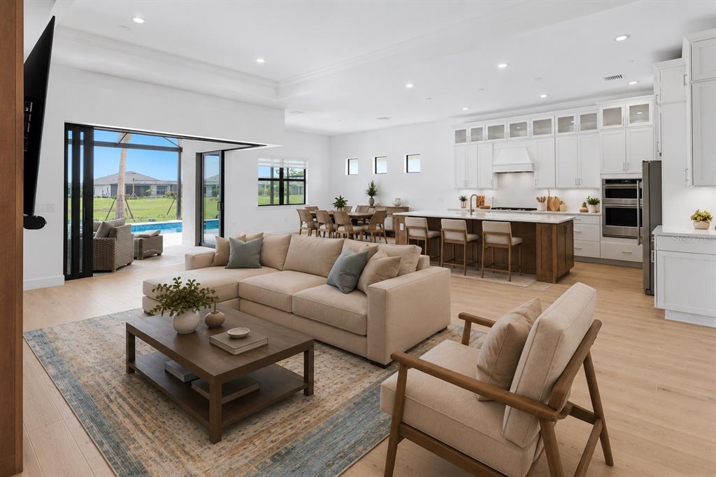 An open-concept living room and kitchen with light wood floors, white cabinetry, and sliding glass doors — 4923 EMPIRE LANDING RUN, BRADENTON, FL