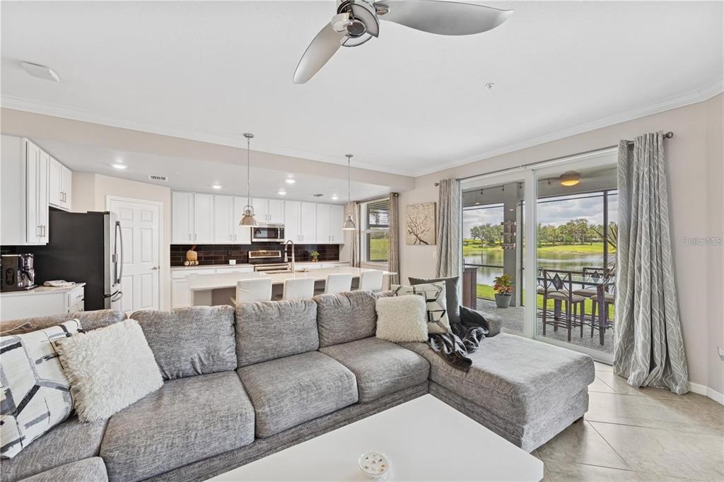A living room with a gray sectional sofa opens to a kitchen and a lake view — 917 TIDEWATER SHORES LOOP, BRADENTON, FL