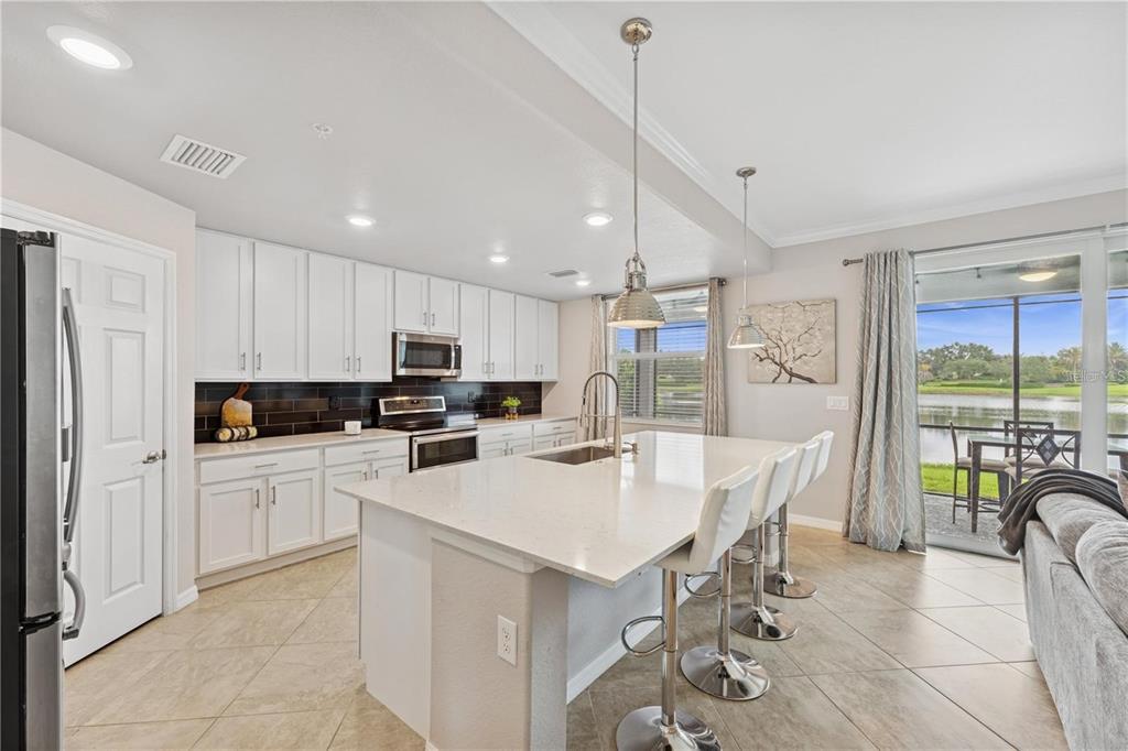A kitchen with white cabinets, a quartz island, and a view of a lake outside — 917 TIDEWATER SHORES LOOP, BRADENTON, FL