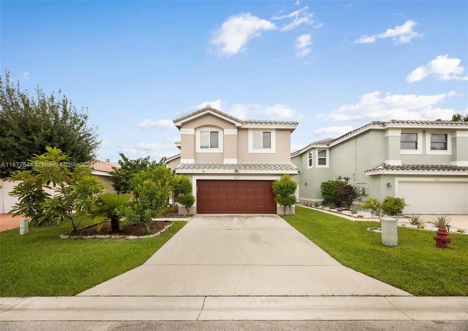 A two-story suburban house features a red garage door, a concrete driveway, and green landscaping — 8317 Bermuda Sound Way, Boynton Beach FL 33436, BOYNTON BEACH, FL