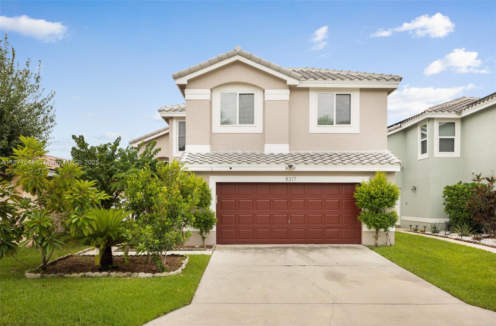 A two-story house features a tan stucco exterior, a red garage door, and a driveway — 8317 Bermuda Sound Way, Boynton Beach FL 33436, BOYNTON BEACH, FL