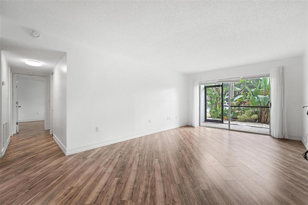 An empty living room features wood-look flooring, white walls, and a sliding glass door — 3223 BENEVA ROAD UNIT 101, SARASOTA, FL