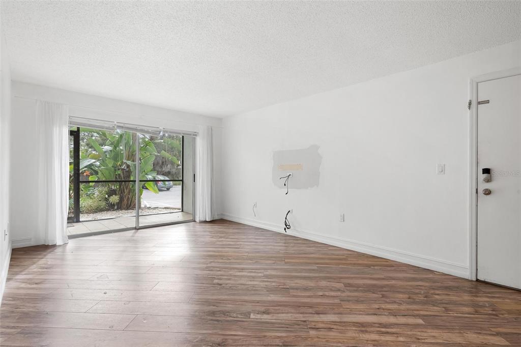 An empty living room features wood-look flooring, white walls, and a sliding glass door — 3223 BENEVA ROAD UNIT 101, SARASOTA, FL