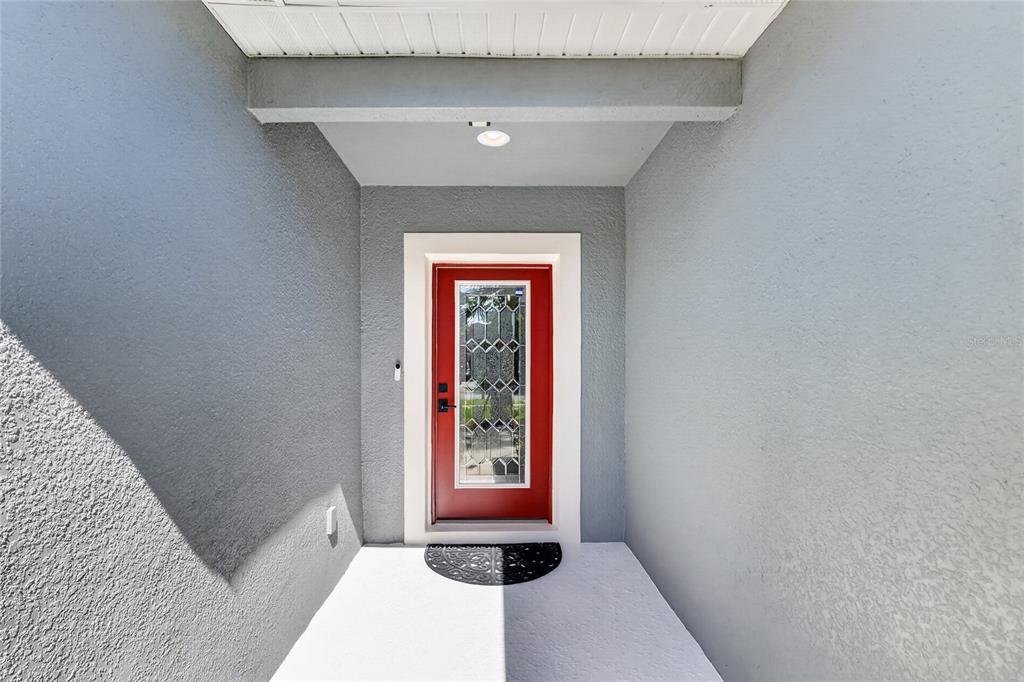 A red front door with a glass insert is centered in a gray stucco entryway — 345 RED KITE DRIVE, GROVELAND, FL