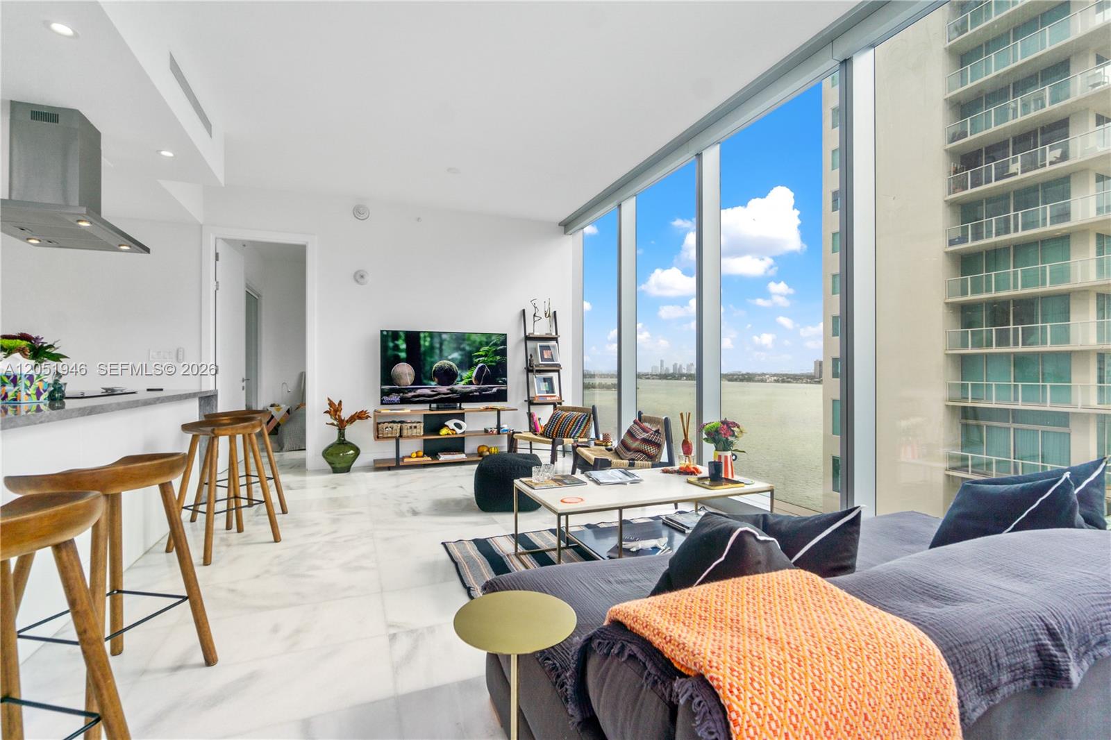 A modern living room features marble floors, floor-to-ceiling windows, and a view of water — 700 NE 26th Ter # 1005, Miami FL 33137, MIAMI, FL