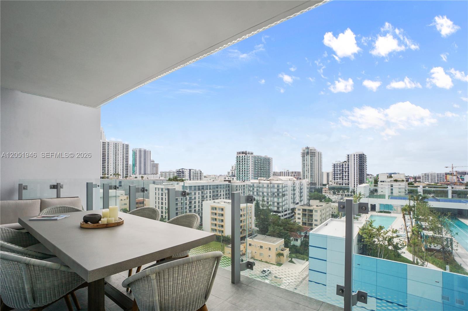 A balcony features a dining table and chairs overlooking a city skyline and pool — 700 NE 26th Ter # 1005, Miami FL 33137, MIAMI, FL