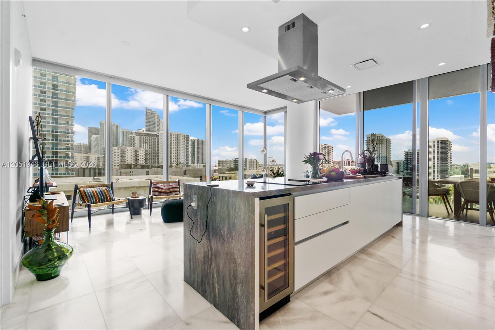 A modern kitchen island with a wine cooler sits in a room with floor-to-ceiling windows — 700 NE 26th Ter # 1005, Miami FL 33137, MIAMI, FL
