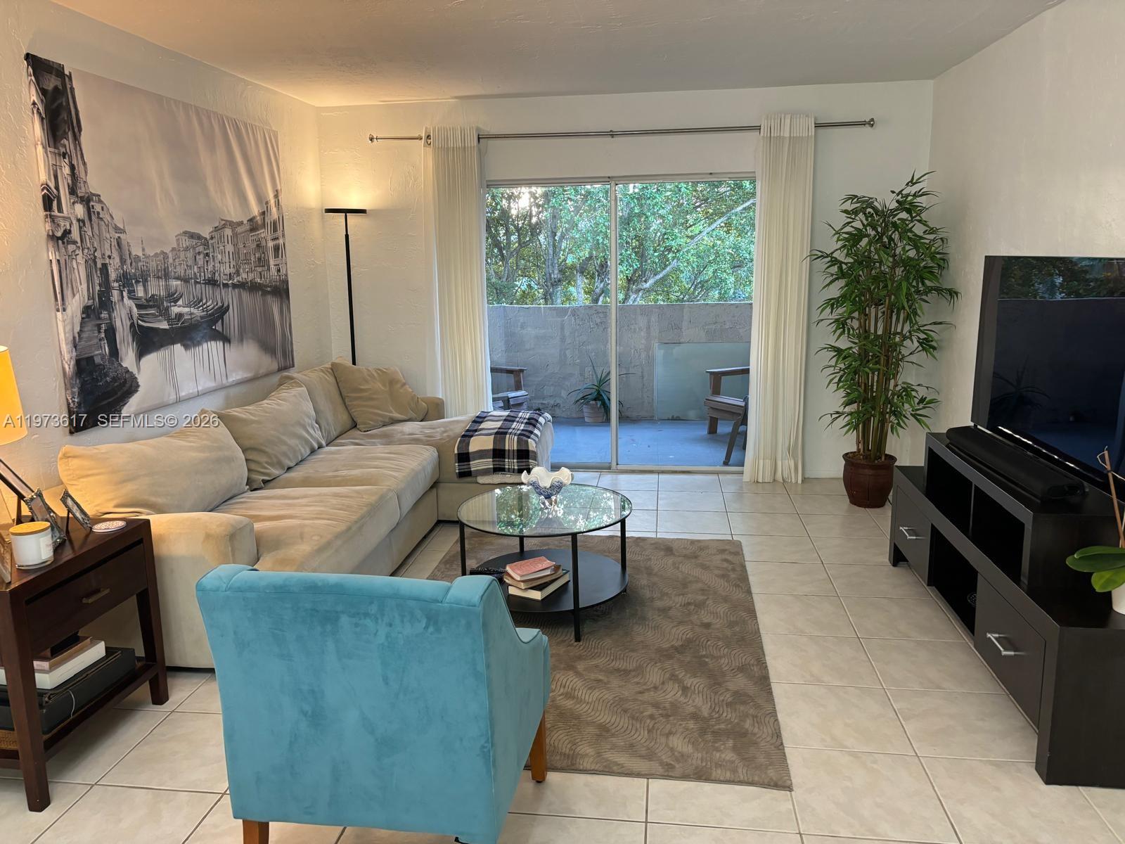A living room features a sectional sofa, a blue armchair, a glass coffee table, and a balcony — 6884 N Kendall Dr # C407, Pinecrest FL 33156, PINECREST, FL