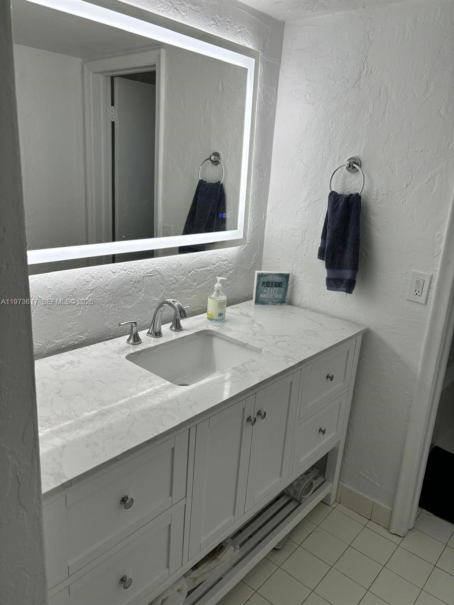 A bathroom features a white vanity with a marble countertop, a sink, and an illuminated mirror — 6884 N Kendall Dr # C407, Pinecrest FL 33156, PINECREST, FL