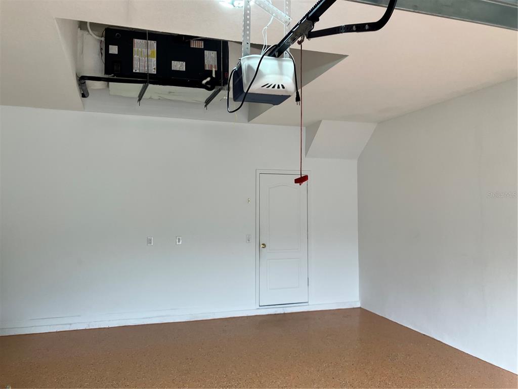 A garage interior features a white door, a ceiling-mounted garage door opener, and an HVAC unit — 15041 PRINCEWOOD LANE, LAND O LAKES, FL