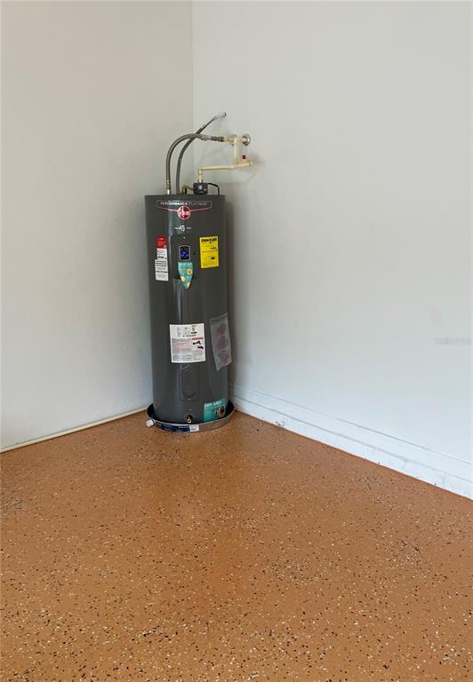A Rheem electric water heater sits in the corner of a garage with speckled flooring — 15041 PRINCEWOOD LANE, LAND O LAKES, FL