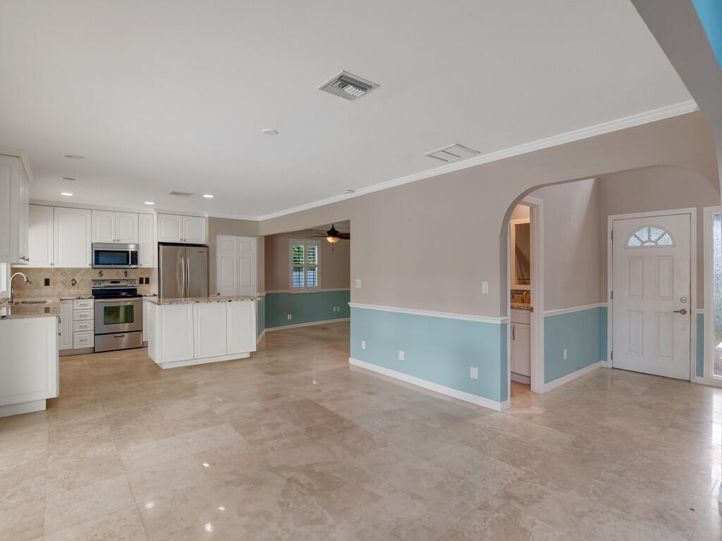 A kitchen with white cabinets and stainless steel appliances opens to a light-filled living area — 721 Shore Drive, Vero Beach FL 32963, VERO BEACH, FL