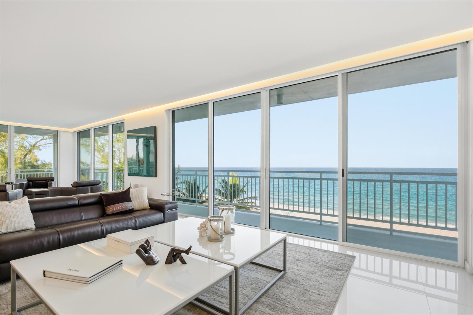 A modern living room features a dark leather sofa, white coffee tables, and floor-to-ceiling windows — 2150 N Ocean Blvd, Boca Raton FL 33431, BOCA RATON, FL