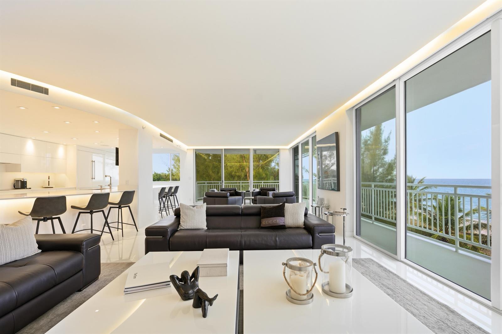 A modern living room with dark leather sofas, white coffee tables, and floor-to-ceiling ocean views — 2150 N Ocean Blvd, Boca Raton FL 33431, BOCA RATON, FL