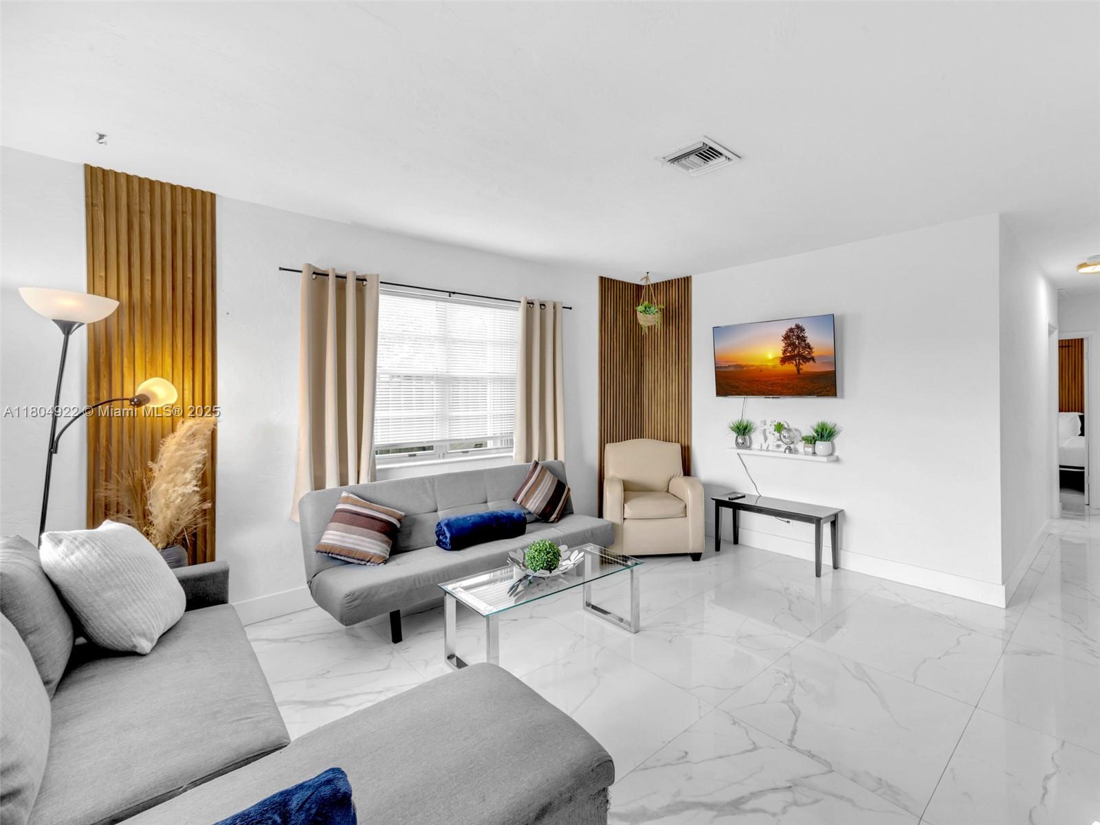A living room features a grey sofa, a glass coffee table, and wood-slat wall accents — 421 W Pembroke Rd # 0, Hallandale Beach FL 33009, HALLANDALE BEACH, FL