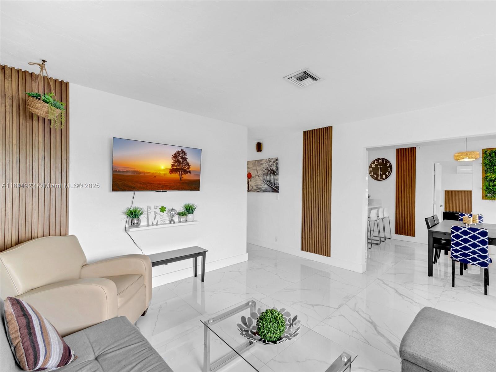 A living room features white tile floors, wood slat wall accents, and a wall-mounted television — 421 W Pembroke Rd # 0, Hallandale Beach FL 33009, HALLANDALE BEACH, FL
