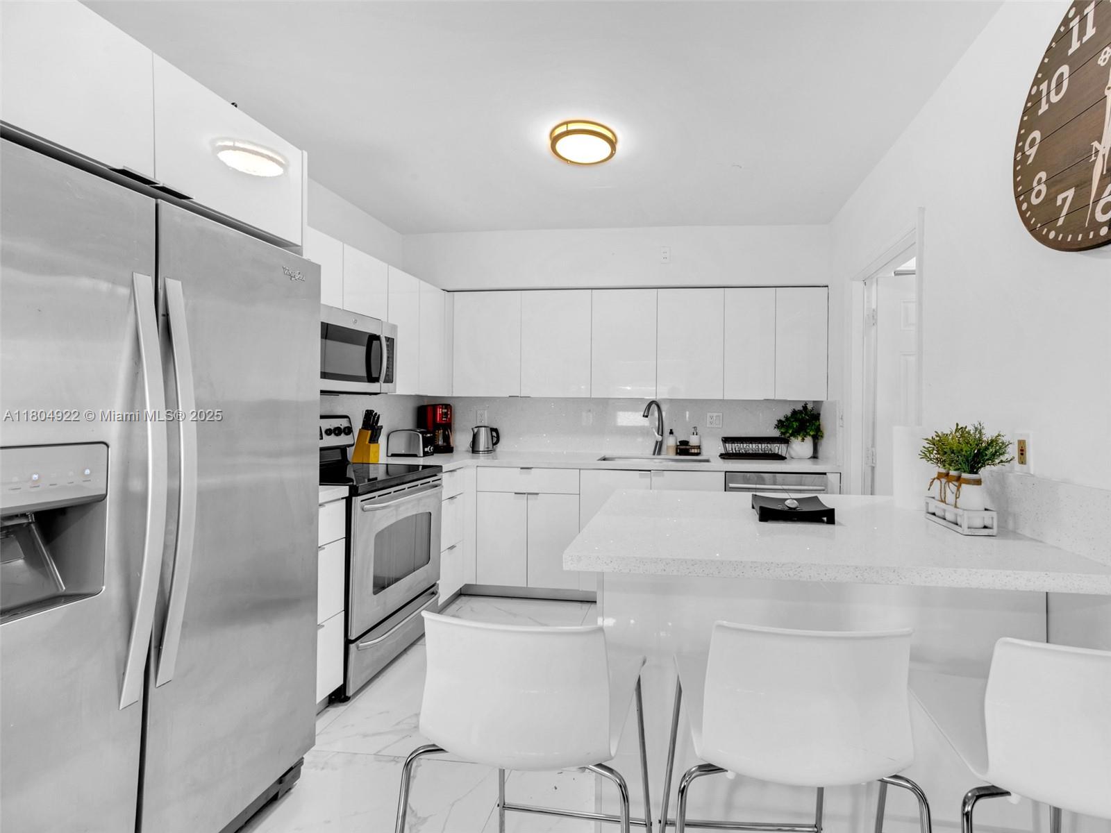 A modern kitchen features white cabinets, stainless steel appliances, and a white quartz breakfast bar — 421 W Pembroke Rd # 0, Hallandale Beach FL 33009, HALLANDALE BEACH, FL