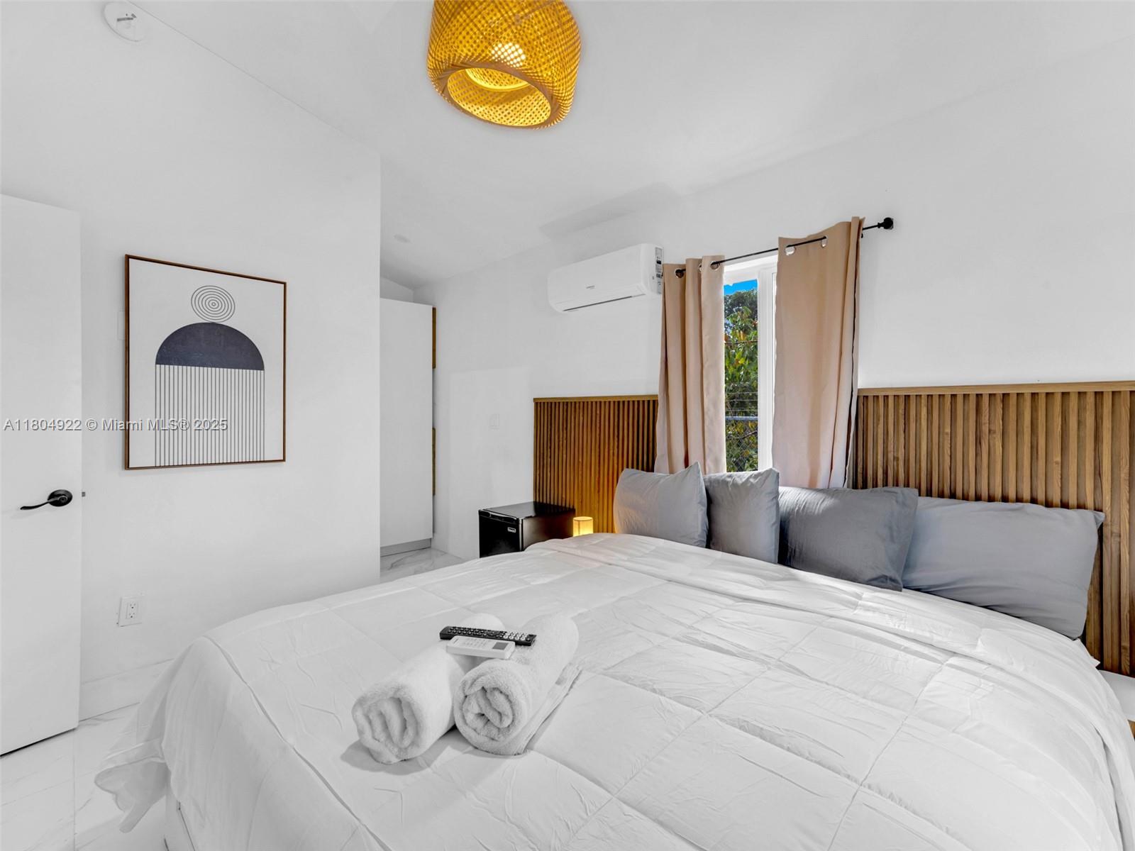 A bedroom features a bed with white bedding, a wooden headboard, and a woven light fixture — 421 W Pembroke Rd # 0, Hallandale Beach FL 33009, HALLANDALE BEACH, FL