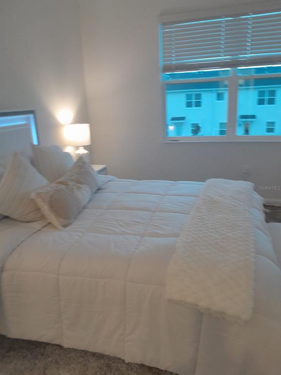 A bedroom features a white bed with a textured throw blanket and a bedside lamp — 113 BOGEY DRIVE, DAVENPORT, FL