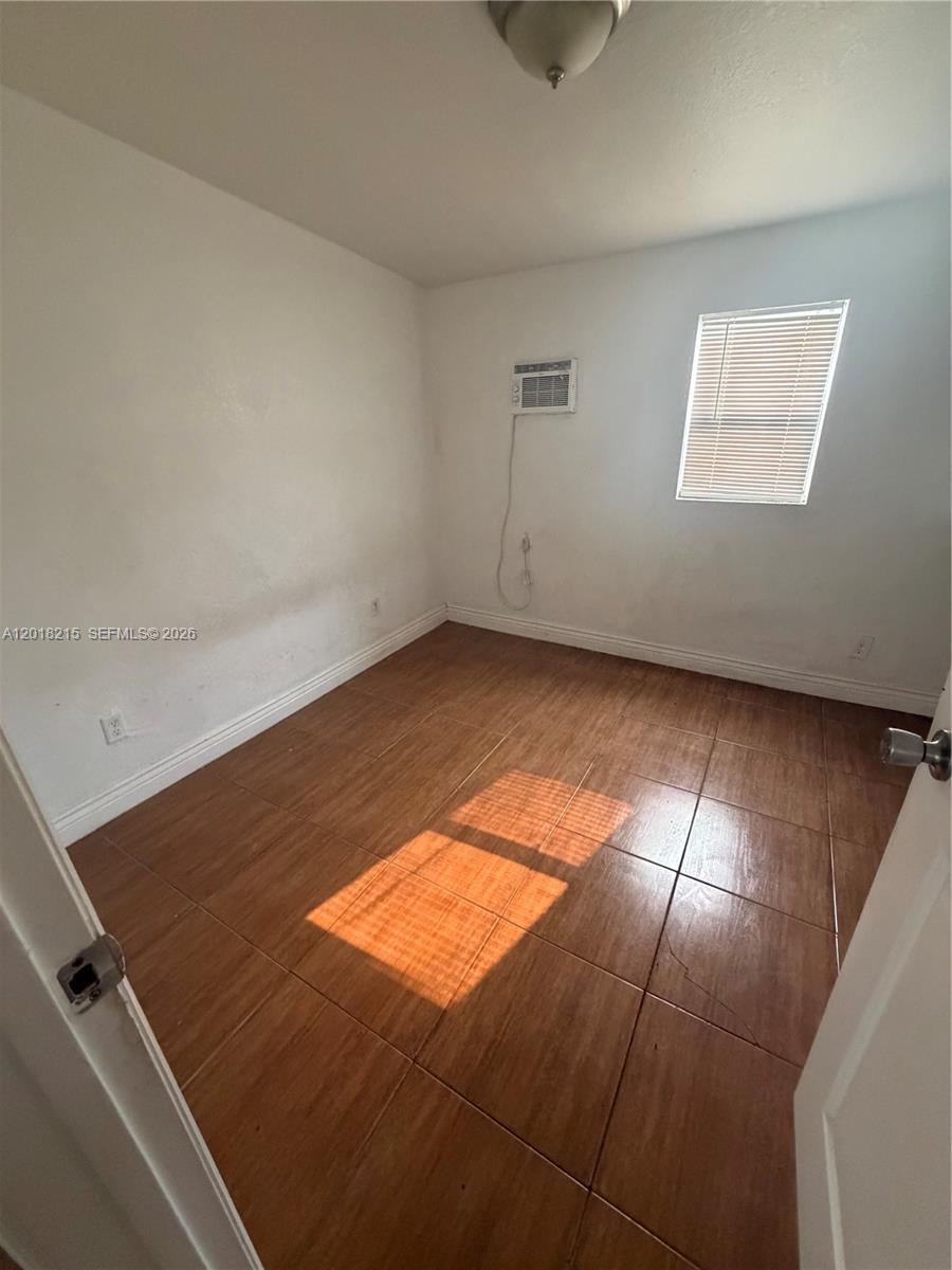 An empty bedroom features light-colored walls, brown tiled flooring, a window, and a wall-mounted air conditioner — 410 N 58th Ave # 408, Hollywood FL 33021, HOLLYWOOD, FL
