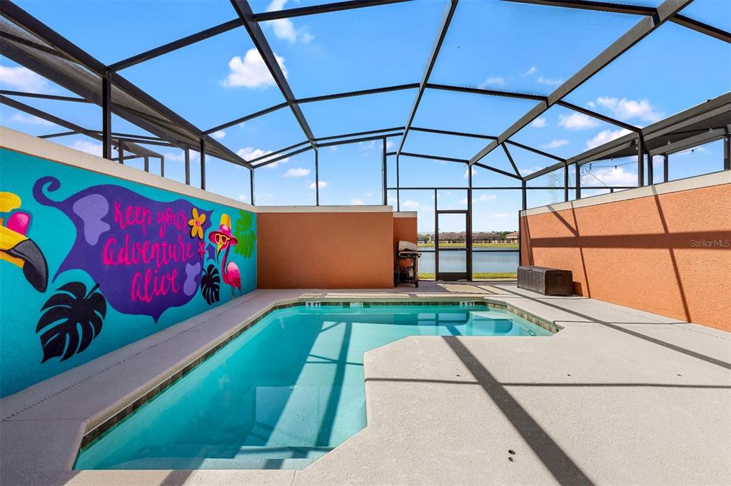 A screened-in pool area features a mural on the wall and a view of water — 8928 CUBAN PALM ROAD, KISSIMMEE, FL