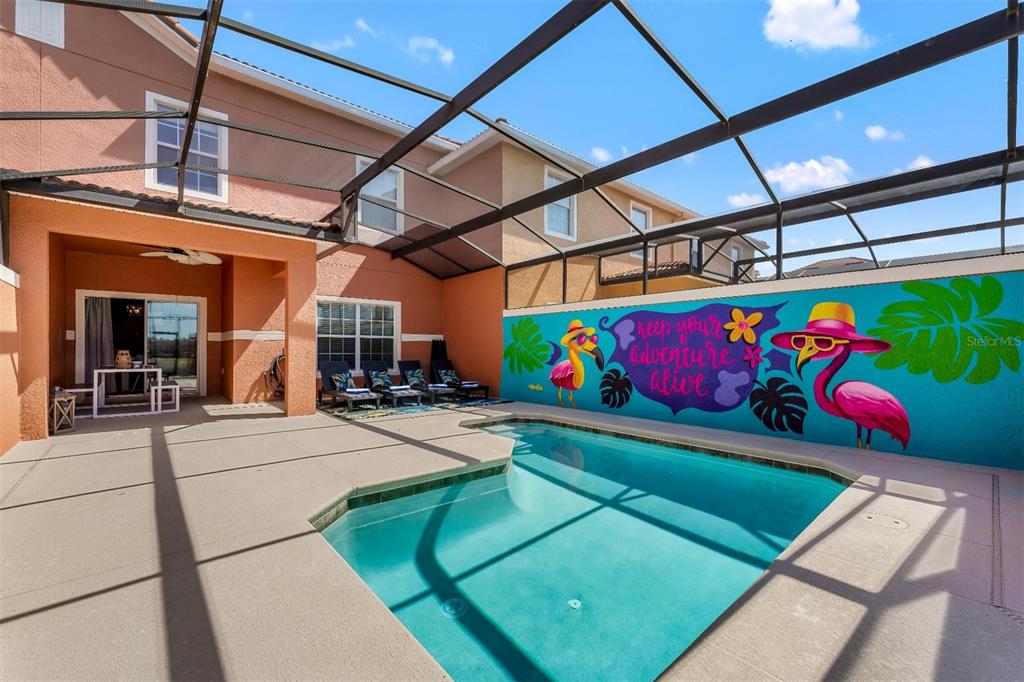 A screened-in swimming pool patio features a colorful flamingo mural on the back wall — 8928 CUBAN PALM ROAD, KISSIMMEE, FL