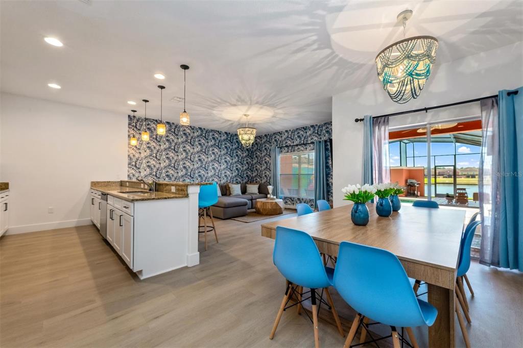 An open-concept dining and living area features blue patterned wallpaper, bright blue chairs, and lighting — 8928 CUBAN PALM ROAD, KISSIMMEE, FL