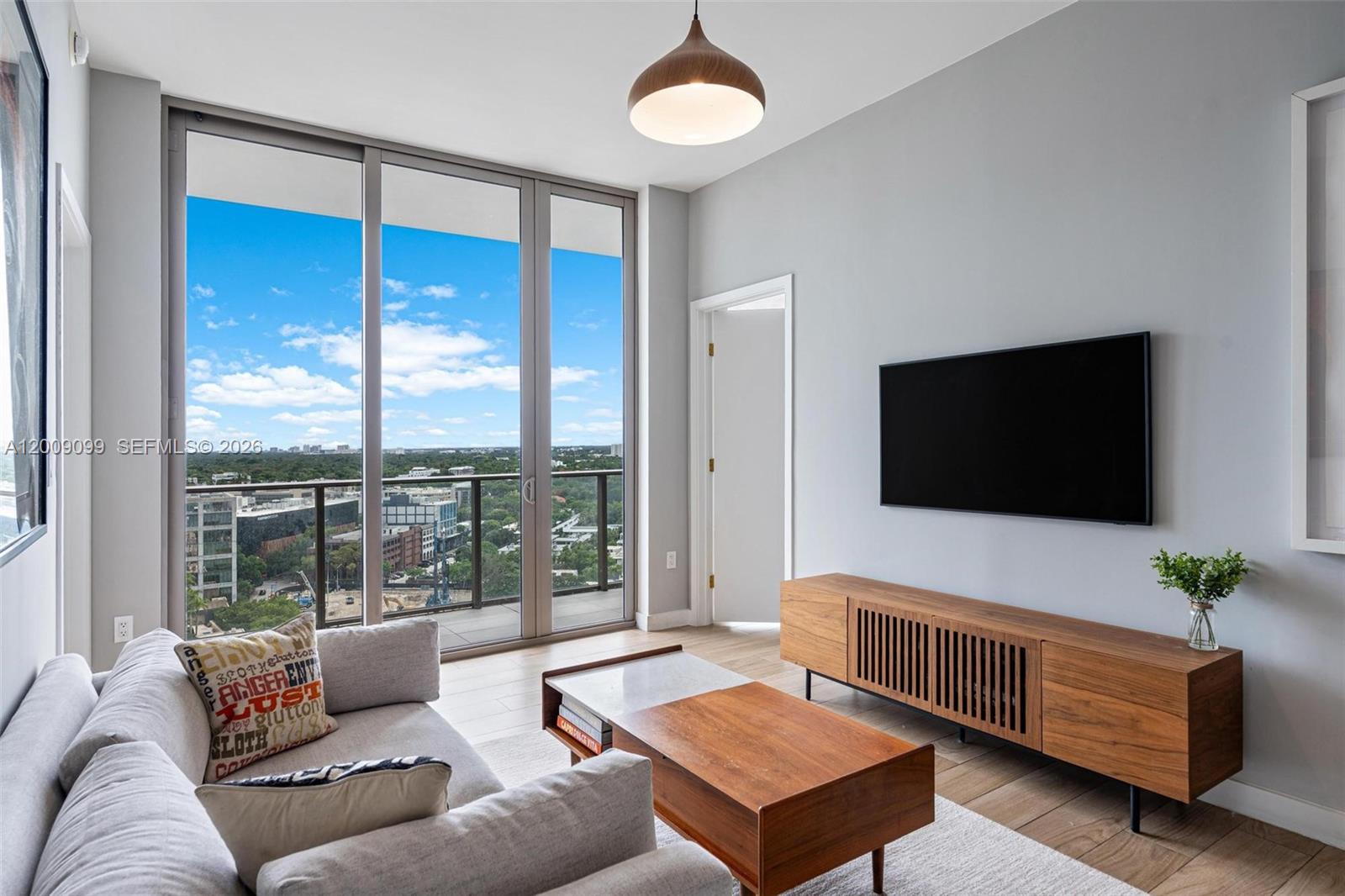 A modern living room features a wall-mounted television, wooden media console, and floor-to-ceiling balcony windows — 2678 Tigertail # 1603, Miami FL 33133, MIAMI, FL