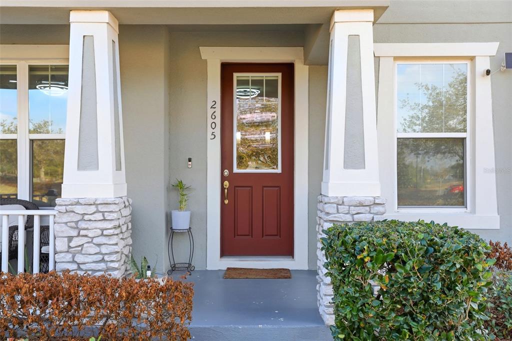 A front porch features a red door with a glass pane and stone-based columns — 2605 PLAY HARD ALLEY, KISSIMMEE, FL