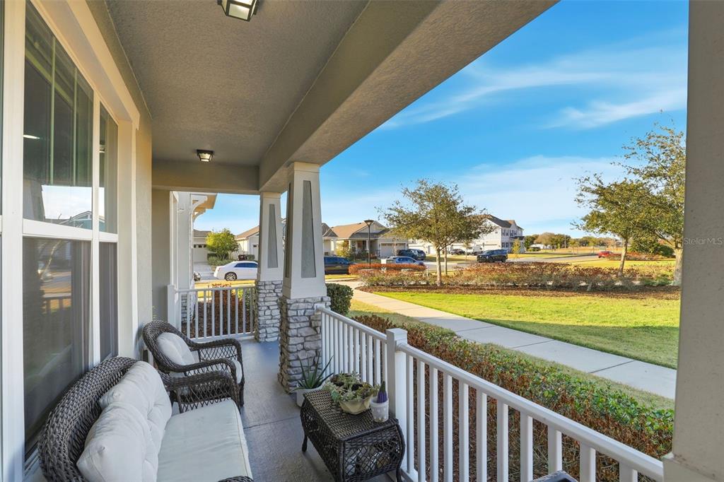 A covered front porch features wicker furniture, white railings, and a view of the neighborhood — 2605 PLAY HARD ALLEY, KISSIMMEE, FL