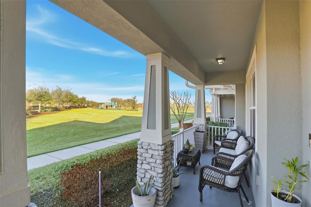 A covered front porch with wicker furniture overlooks a grassy park with a playground — 2605 PLAY HARD ALLEY, KISSIMMEE, FL