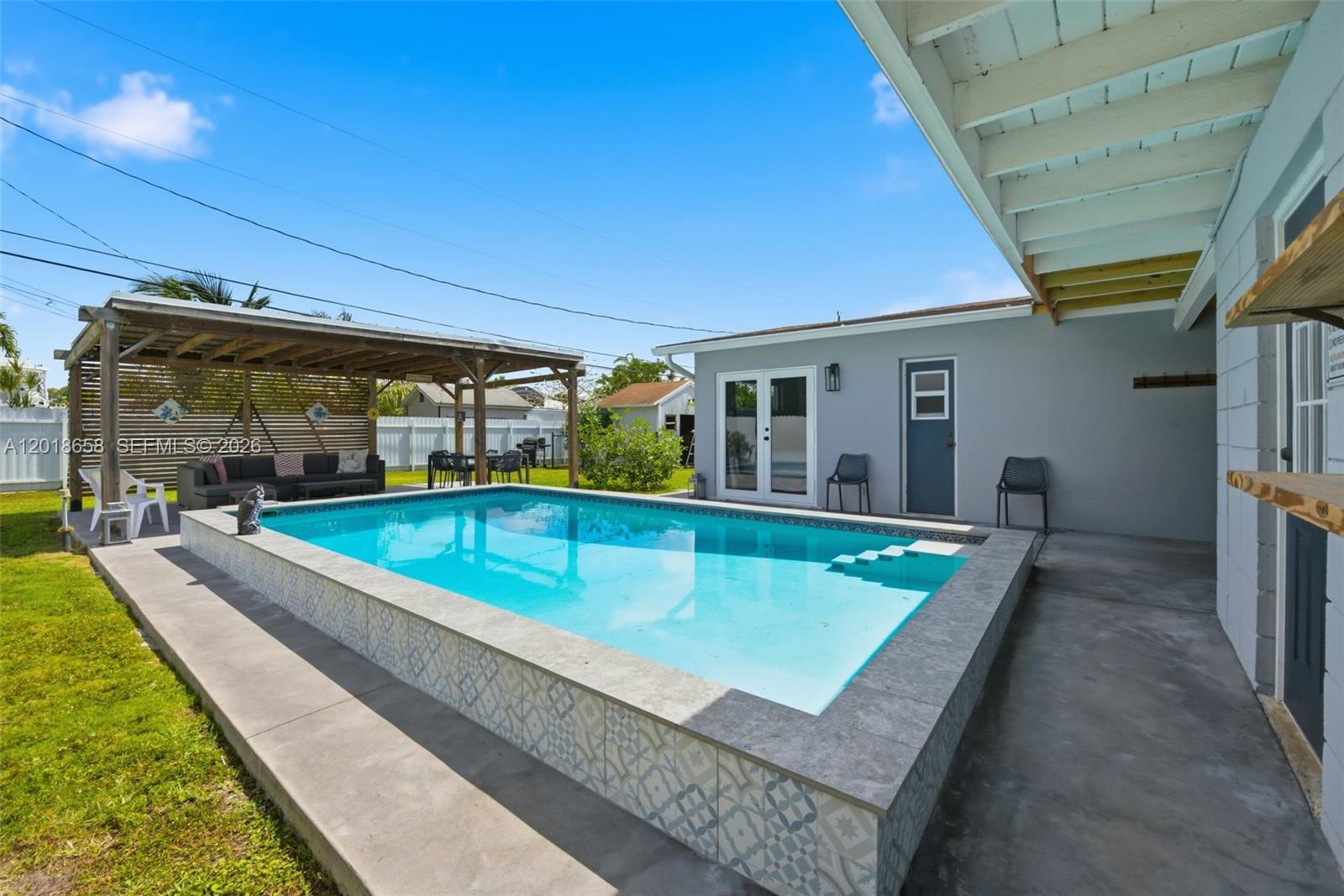 A backyard features an above-ground swimming pool with patterned tile siding and a wooden pergola — 9955 SW 215th St, Cutler Bay FL 33189, CUTLER BAY, FL