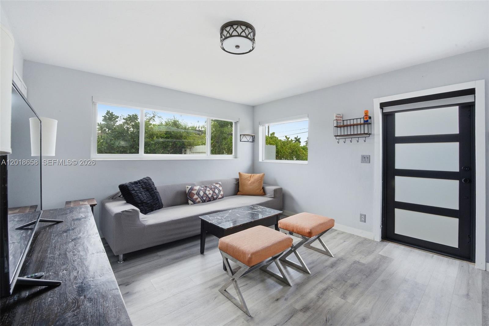 A living room features a grey sofa, marble coffee table, two orange ottomans, and light flooring — 9955 SW 215th St, Cutler Bay FL 33189, CUTLER BAY, FL