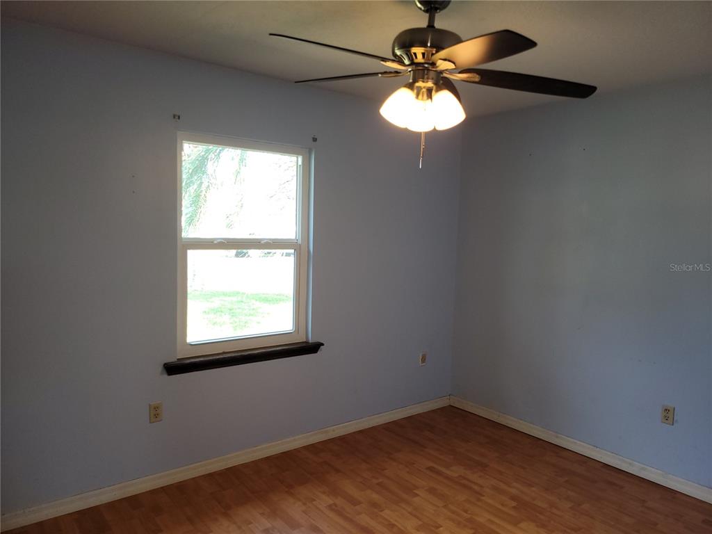 An empty bedroom features light blue walls, wood-look flooring, a window, and a ceiling fan — 726 DIPLOMAT AVENUE SE, PALM BAY, FL