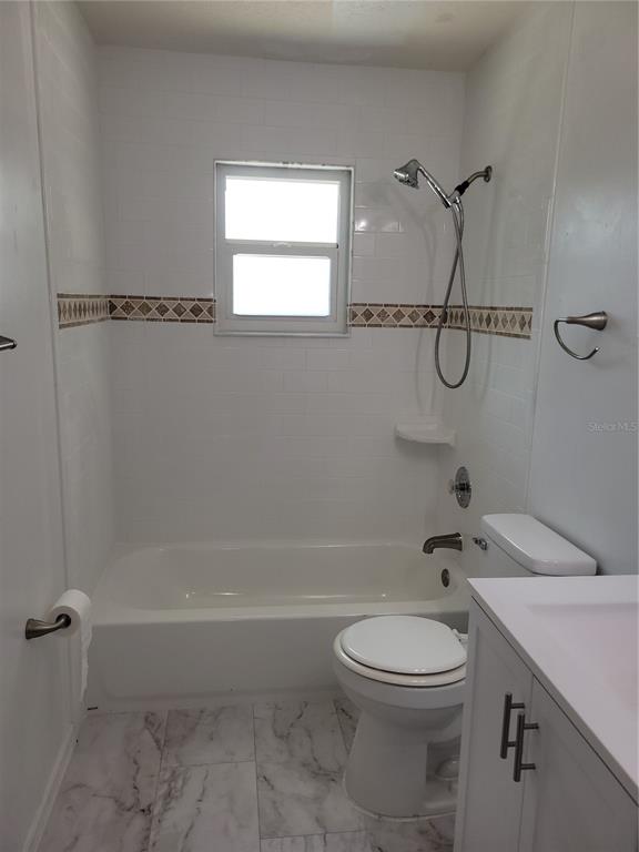 A bathroom features a white tub-shower combination, a toilet, and a vanity with marble-look flooring — 726 DIPLOMAT AVENUE SE, PALM BAY, FL