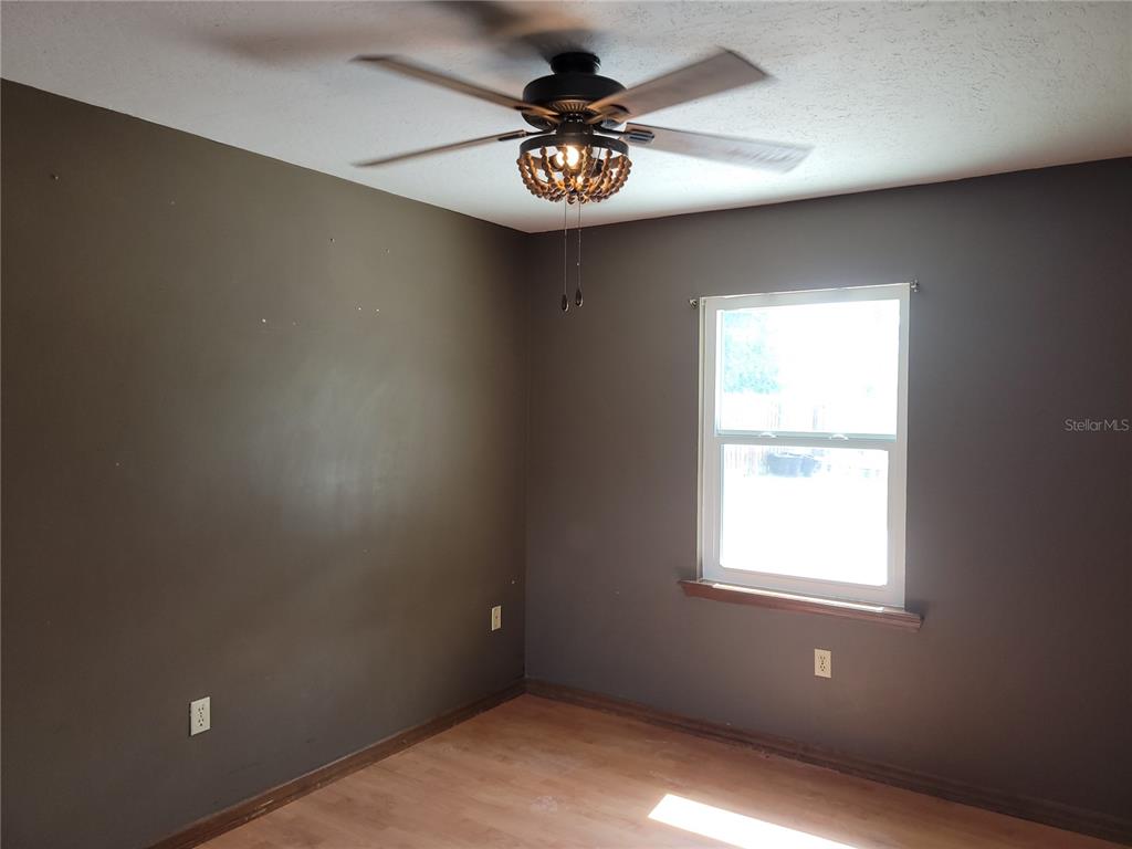 A bedroom with dark brown walls, wood-look flooring, and a beaded ceiling fan light fixture — 726 DIPLOMAT AVENUE SE, PALM BAY, FL